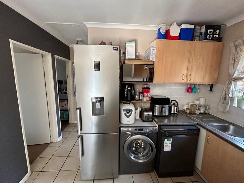 A functional kitchen area featuring built-in cabinetry, laminate countertops, a stainless steel sink, and tiled flooring, providing essential utility space.