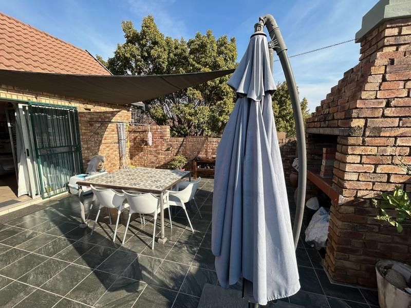 Outdoor patio area featuring a built-in brick braai, tiled flooring, and a shade sail, providing a functional space for outdoor entertaining.