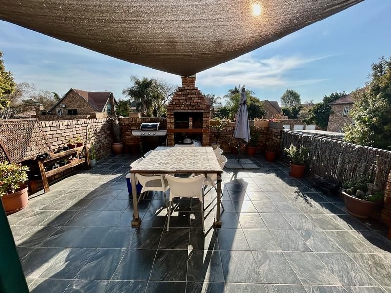 Spacious outdoor patio featuring a built-in brick braai, dark tiled flooring, and a protective shade sail, perfect for alfresco dining and entertaining.