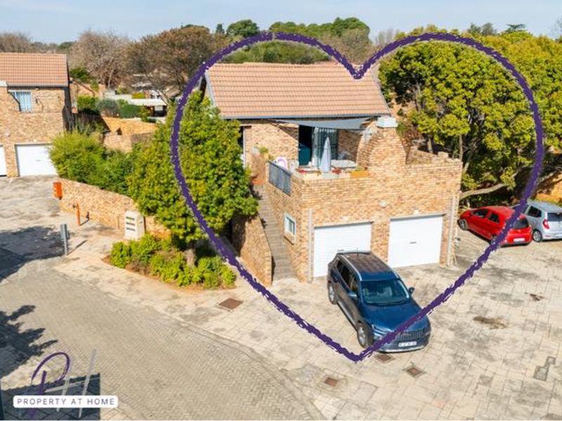 Aerial view of a face-brick townhouse featuring a double garage, external staircase, and an elevated balcony area within a residential complex.