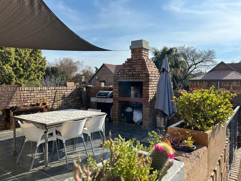 Outdoor patio area featuring a brick built-in braai, tiled flooring, and a shade sail, providing a functional space for outdoor dining and entertainment.