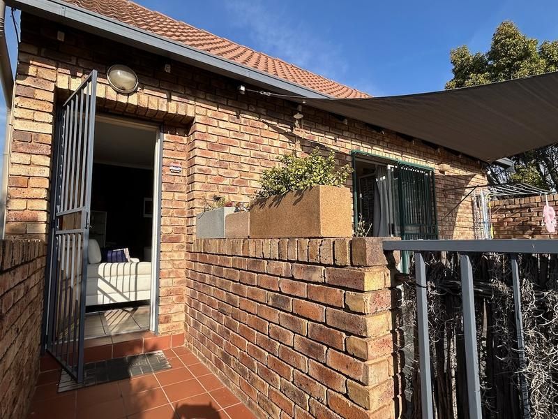 A private brick-walled patio area featuring tiled flooring, a security gate, and a shade sail, providing a functional outdoor space.