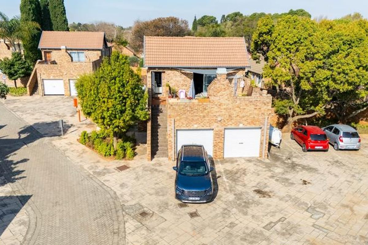 Aerial view of a double-story townhouse featuring a brick facade, tiled roof, double garage, and an external staircase leading to an upper-level balcony.