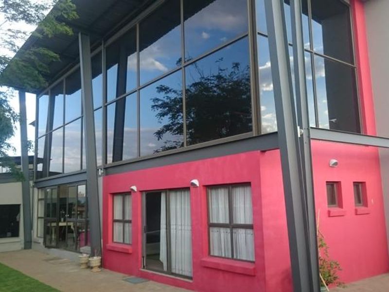 Rear view of a modern home featuring a striking double-volume glass facade, steel structural elements, and a paved patio area.