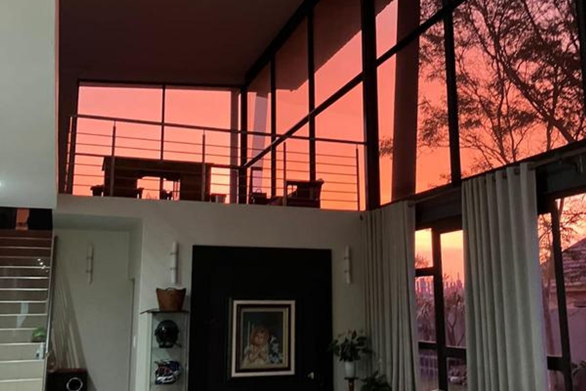Spacious living room featuring double-height floor-to-ceiling windows, a mezzanine level with a stainless steel balustrade, and an open-plan design.