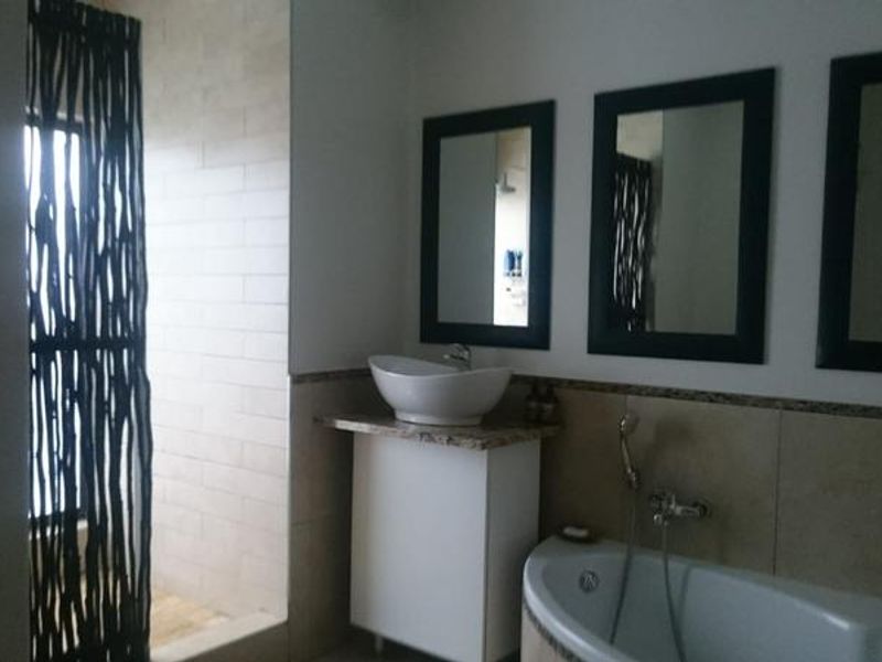 A modern bathroom featuring a corner bathtub, a separate walk-in shower, a vessel sink with a granite vanity, and multiple wall-mounted mirrors.