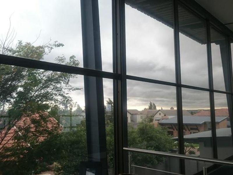 A view from an elevated interior space featuring large floor-to-ceiling aluminium-framed windows and a modern stainless steel balustrade overlooking the surrounding neighbourhood.