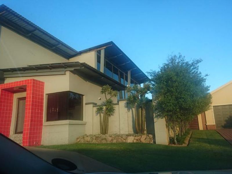 Front elevation of a modern house featuring a distinctive red tiled entrance, metal roofing, paved driveway, and established garden landscaping.