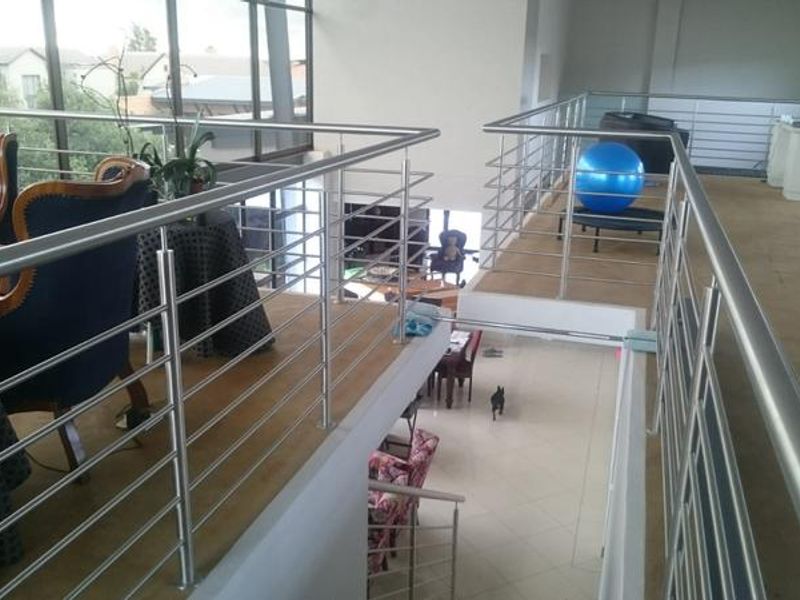 A spacious mezzanine hallway featuring a modern stainless steel balustrade, large windows providing natural light, and views overlooking the lower level living area.