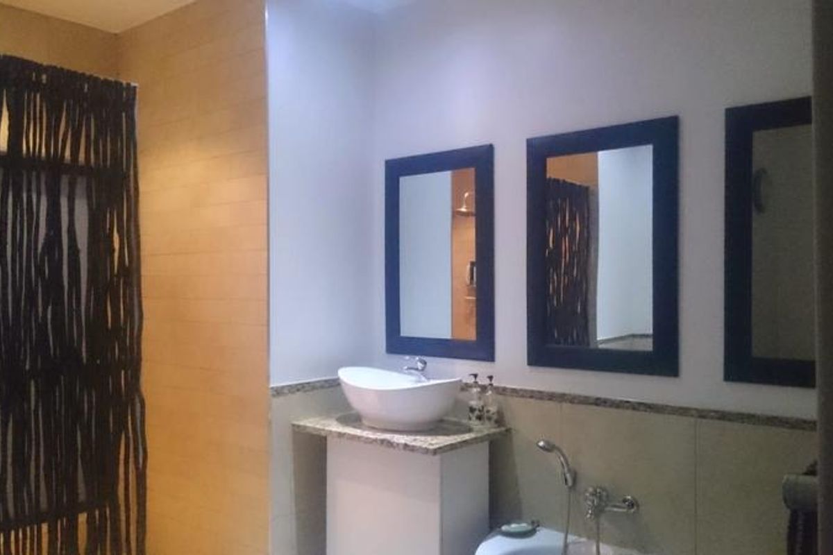 A bathroom featuring a vessel sink on a granite vanity, multiple wall-mounted mirrors, and a shower area.