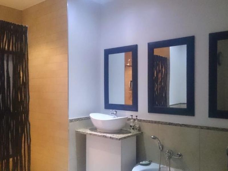 A bathroom featuring a vessel sink on a granite vanity, multiple wall-mounted mirrors, and a shower area.