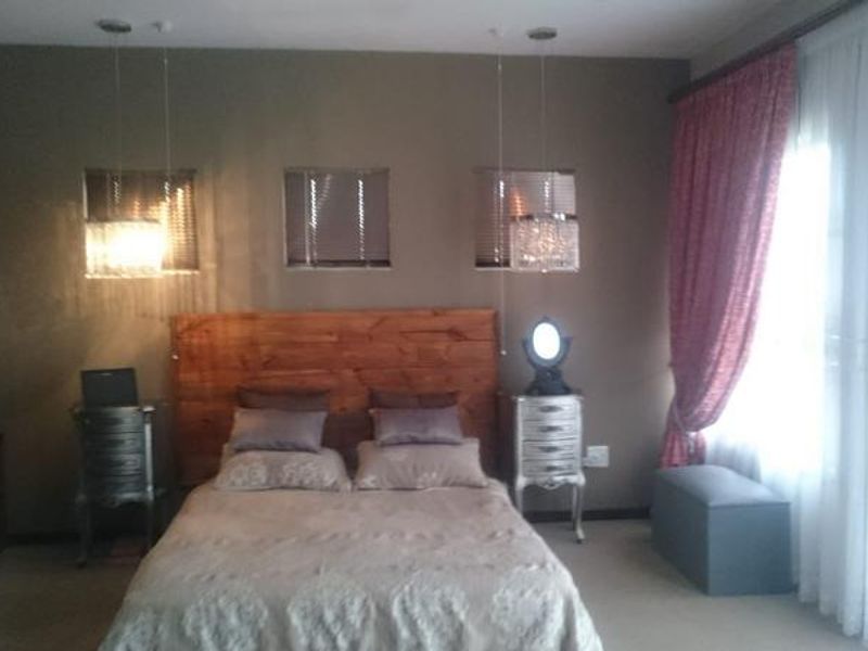 A bedroom featuring a built-in headboard, pendant lighting, and large windows with curtains, offering a functional space with neutral wall tones.