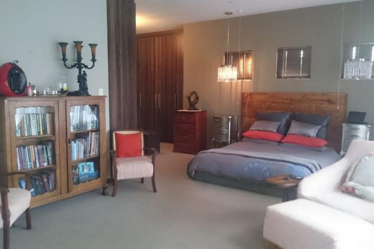 Spacious bedroom featuring built-in cupboards, a timber headboard, and modern pendant lighting, offering a comfortable and well-maintained living space.