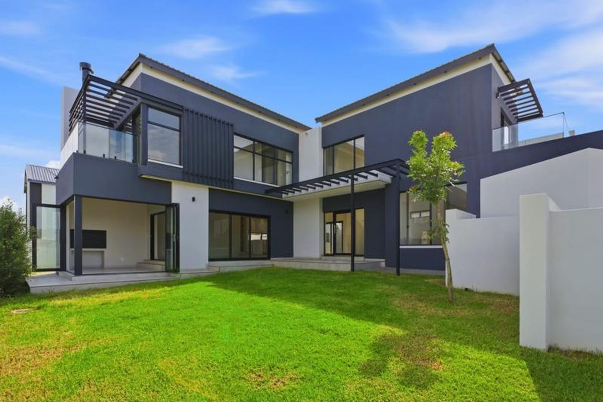 Modern double-story rear elevation featuring a covered patio with built-in braai, upper-level balcony, and landscaped garden area.