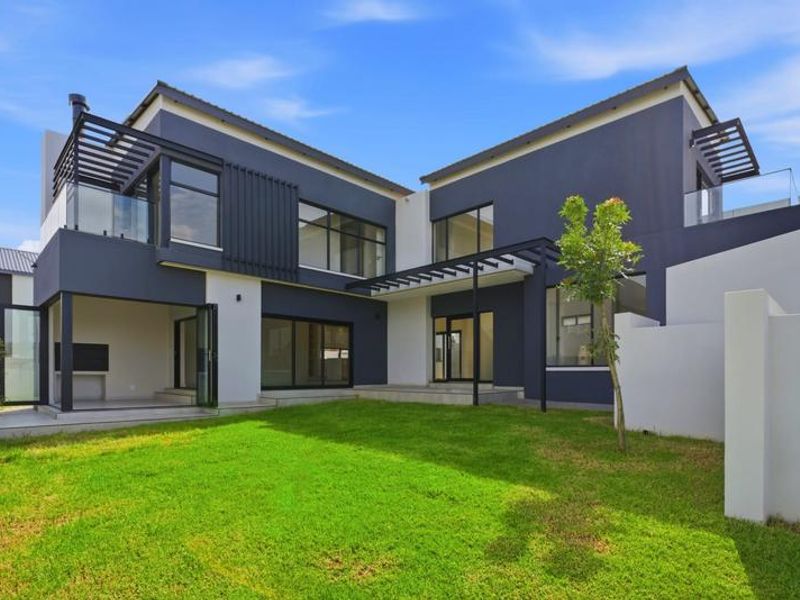 Modern double-story rear elevation featuring a covered patio with built-in braai, upper-level balcony, and landscaped garden area.