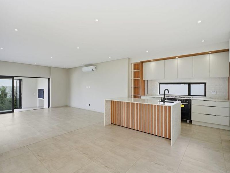Spacious open-plan living and kitchen area featuring modern cabinetry, a central island, tiled floors, and seamless access to an outdoor patio.