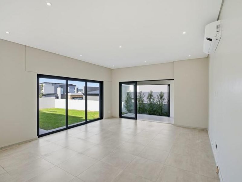 Spacious, modern living area featuring neutral tiled flooring, recessed lighting, split-system air conditioning, and large sliding glass doors opening to the garden.