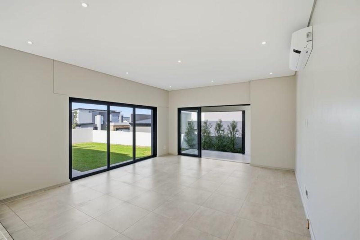 Spacious, modern living area featuring neutral tiled flooring, recessed lighting, split-system air conditioning, and large sliding glass doors opening to the garden.
