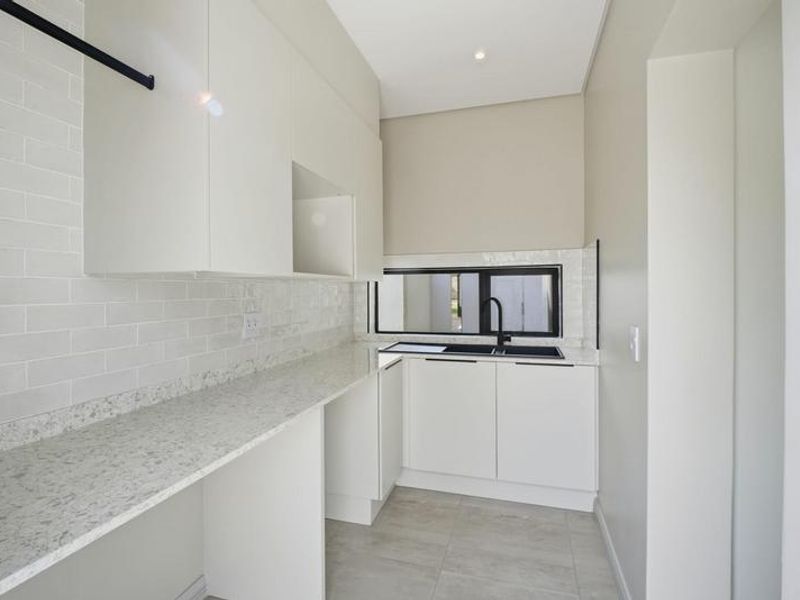 Modern scullery featuring clean white cabinetry, stone countertops, subway tile backsplash, and a sleek black sink fixture.