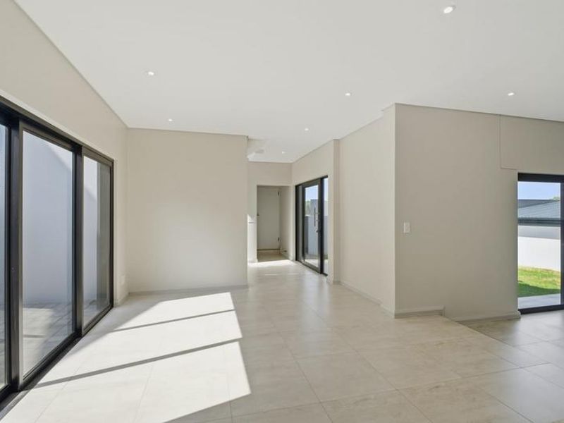 A bright, modern open-plan living space featuring large format floor tiles, recessed downlighting, and expansive aluminium sliding doors leading to the exterior.