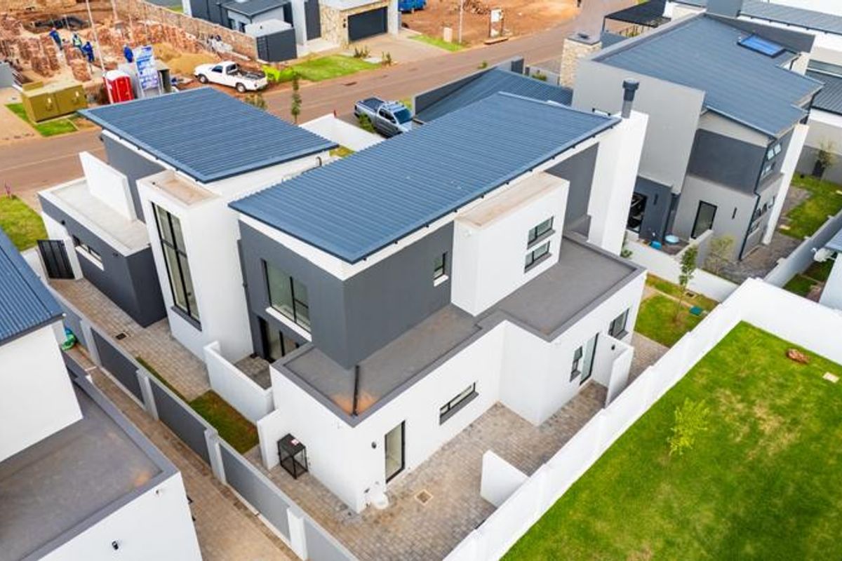 Aerial view of a modern two-story residential property featuring a contemporary design, metal roofing, paved outdoor areas, and a private garden.