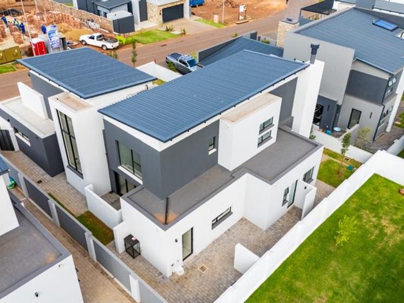 Aerial view of a modern two-story residential property featuring a contemporary design, metal roofing, paved outdoor areas, and a private garden.