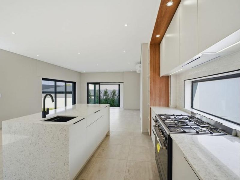 Modern open-plan kitchen featuring a large island, stone countertops, gas hob, and sleek cabinetry, flowing seamlessly into the living area with large sliding doors.