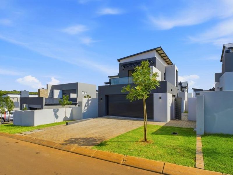 Modern double-story residential home featuring a paved driveway, double garage, and a private balcony with glass balustrades.