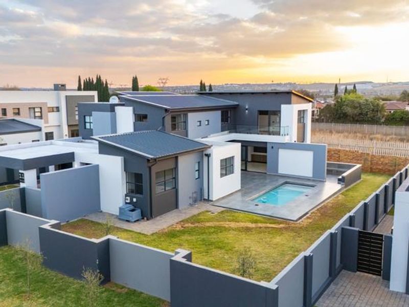 Aerial view of a modern contemporary house featuring a swimming pool, paved patio area, and secure boundary walls in a residential estate.
