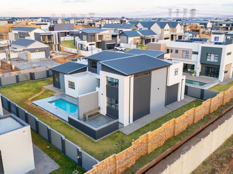 Aerial view of a modern double-story residential property featuring a private swimming pool, paved patio area, and secure boundary walling within a residential estate.