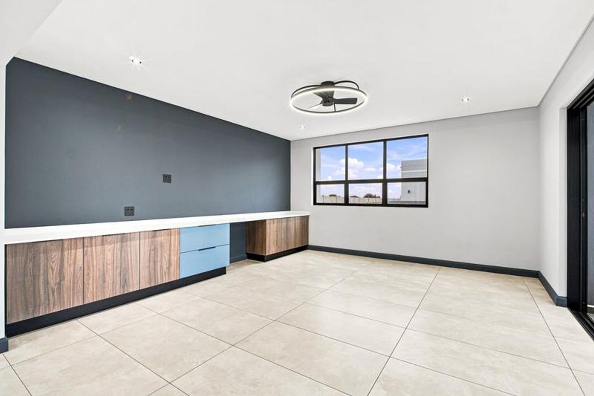 A bright, modern living area featuring neutral tiled flooring, built-in cabinetry with a contemporary finish, and a sleek ceiling fan.