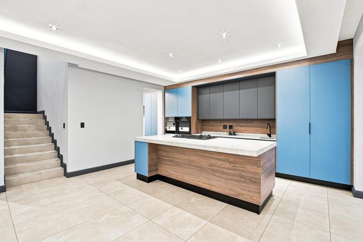 Modern kitchen featuring a central island with a gas hob, integrated cabinetry, stone countertops, and recessed ceiling lighting, adjacent to a staircase.