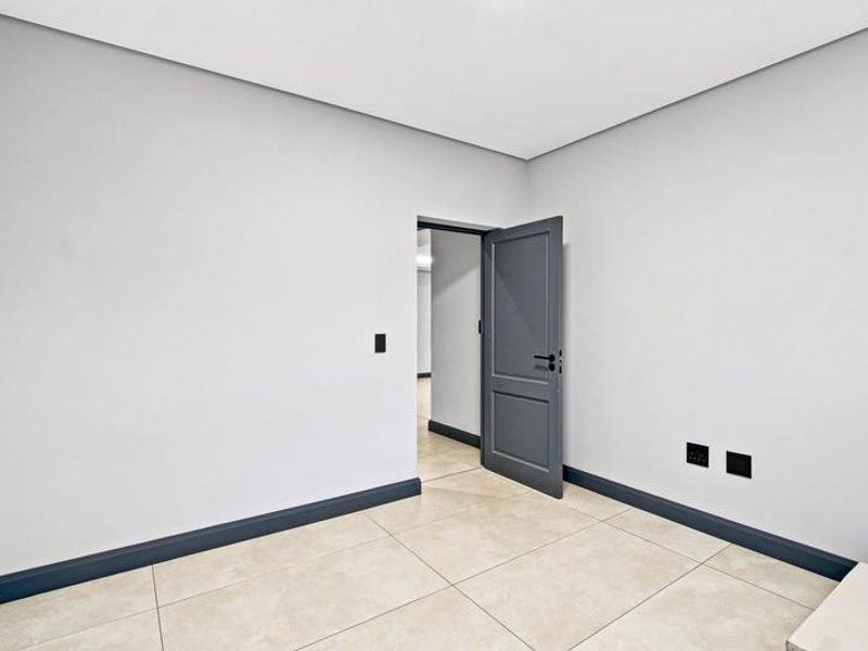 A clean, empty bedroom featuring neutral tiled flooring, modern dark grey skirting boards, and a matching internal door.