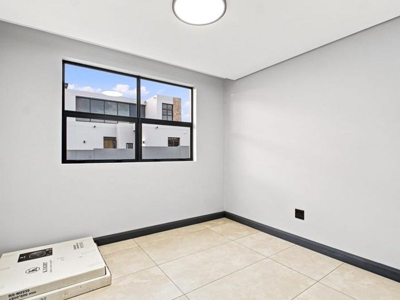 A bright, empty bedroom featuring neutral tiled flooring, clean white walls, and a modern black aluminium window frame.