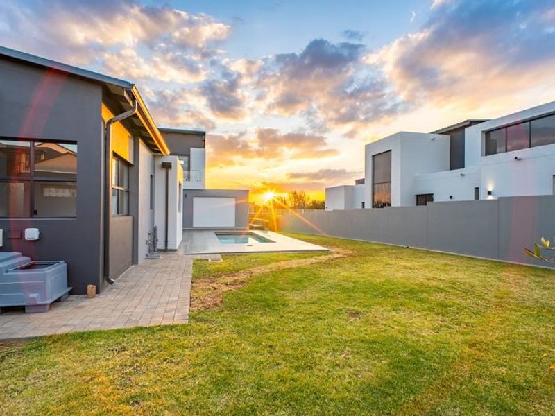 Rear exterior view of a modern home featuring a swimming pool, paved patio area, and a well-maintained lawn at sunset.