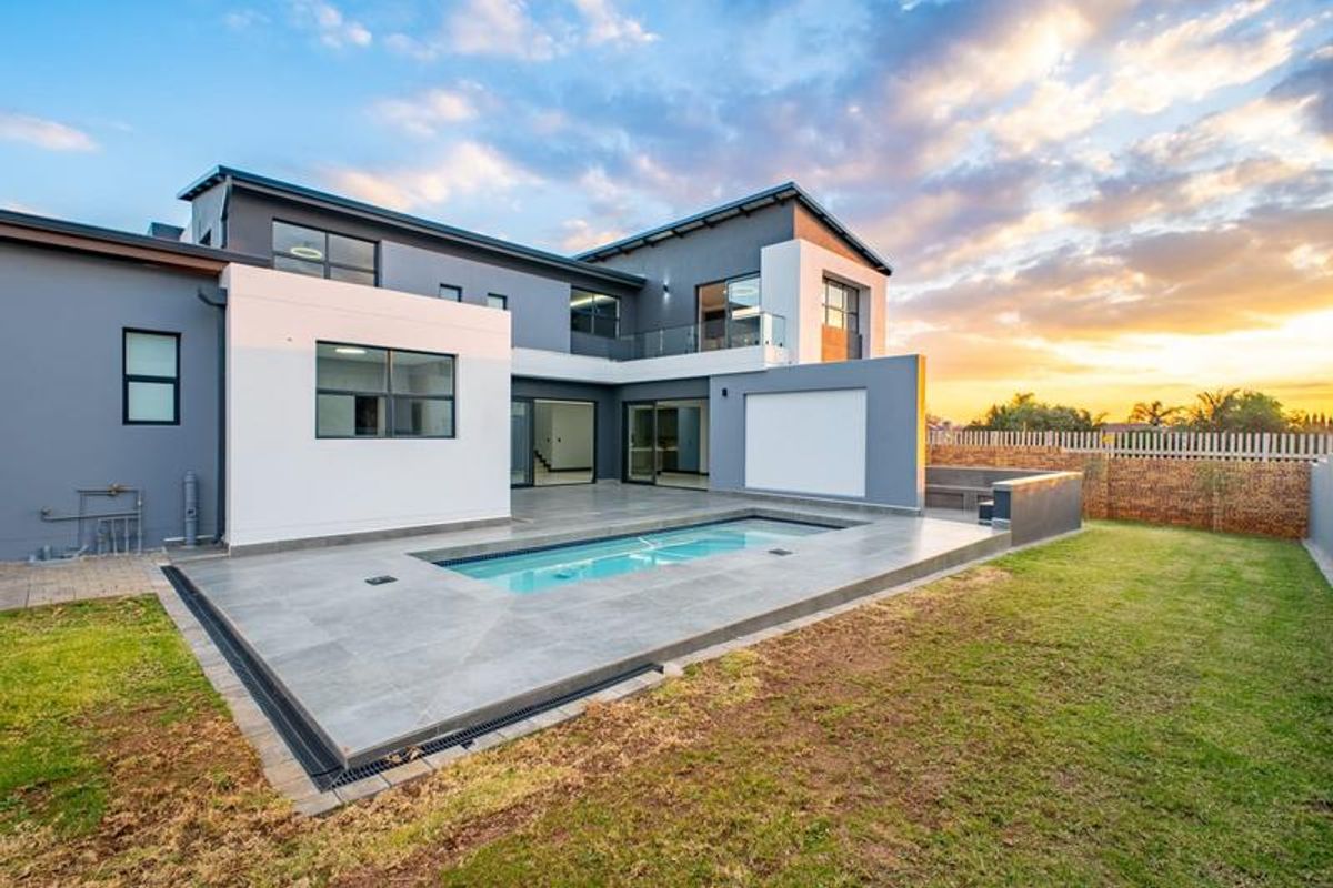 Modern double-story home featuring a rear patio, tiled pool deck, and landscaped garden area at sunset.