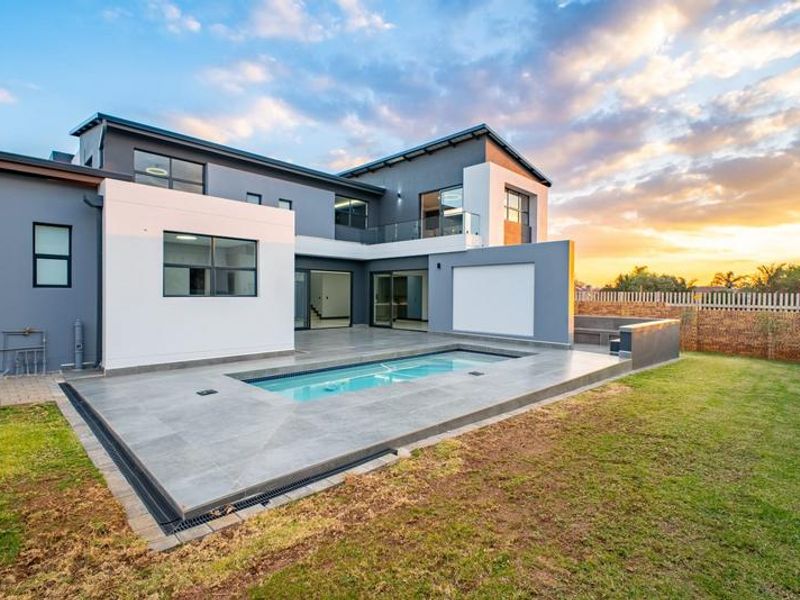 Modern double-story home featuring a rear patio, tiled pool deck, and landscaped garden area at sunset.