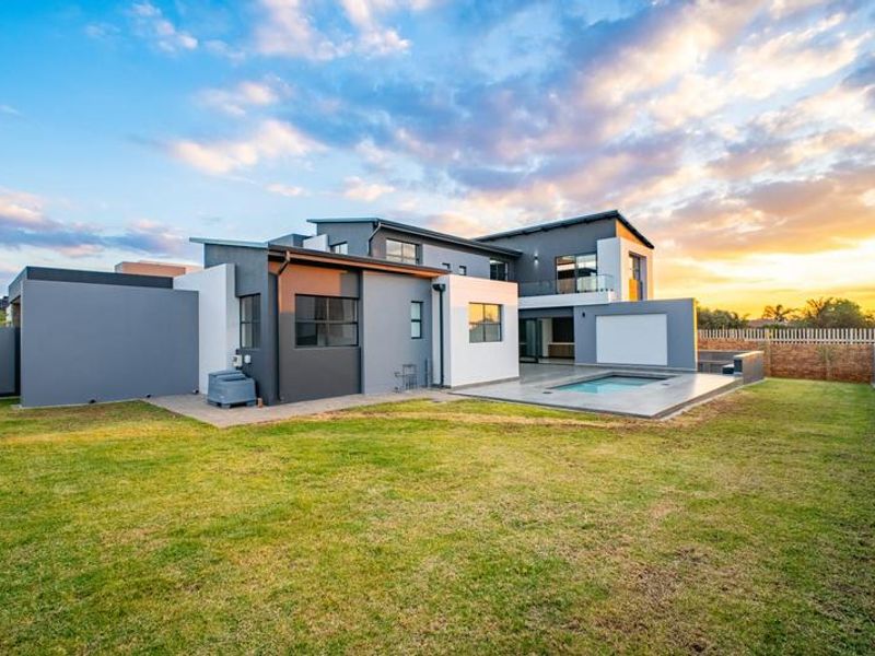 Modern double-story residence featuring a rear garden, paved patio area, and a swimming pool set against a sunset backdrop.