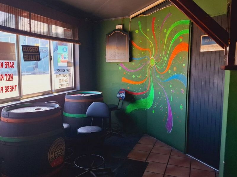 A casual bar area featuring a vibrant painted feature wall, large windows for natural light, and tiled flooring in a commercial setting.