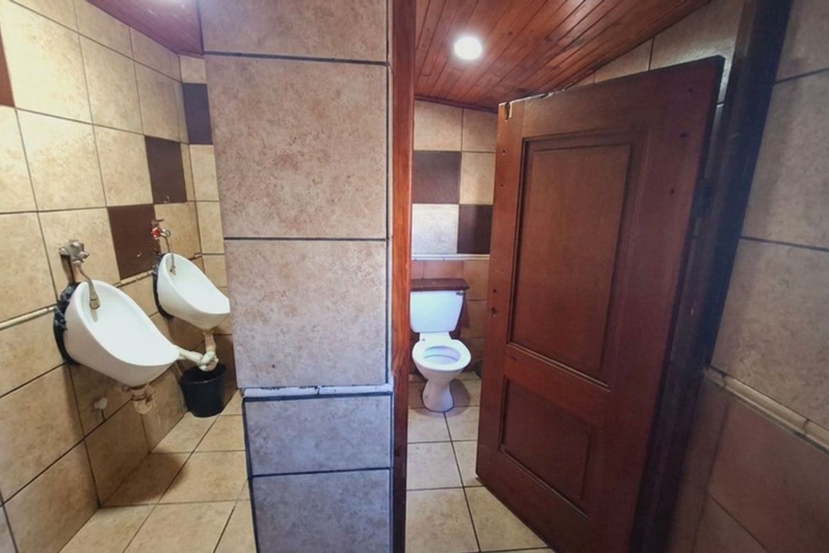 A functional commercial restroom featuring tiled walls and flooring, timber ceiling, two wall-mounted urinals, and a private toilet cubicle.
