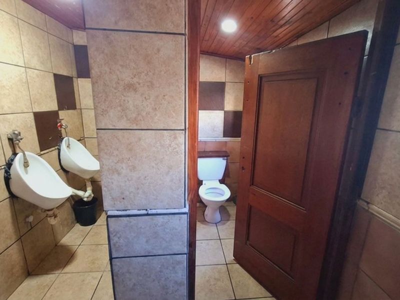 A functional commercial restroom featuring tiled walls and flooring, timber ceiling, two wall-mounted urinals, and a private toilet cubicle.