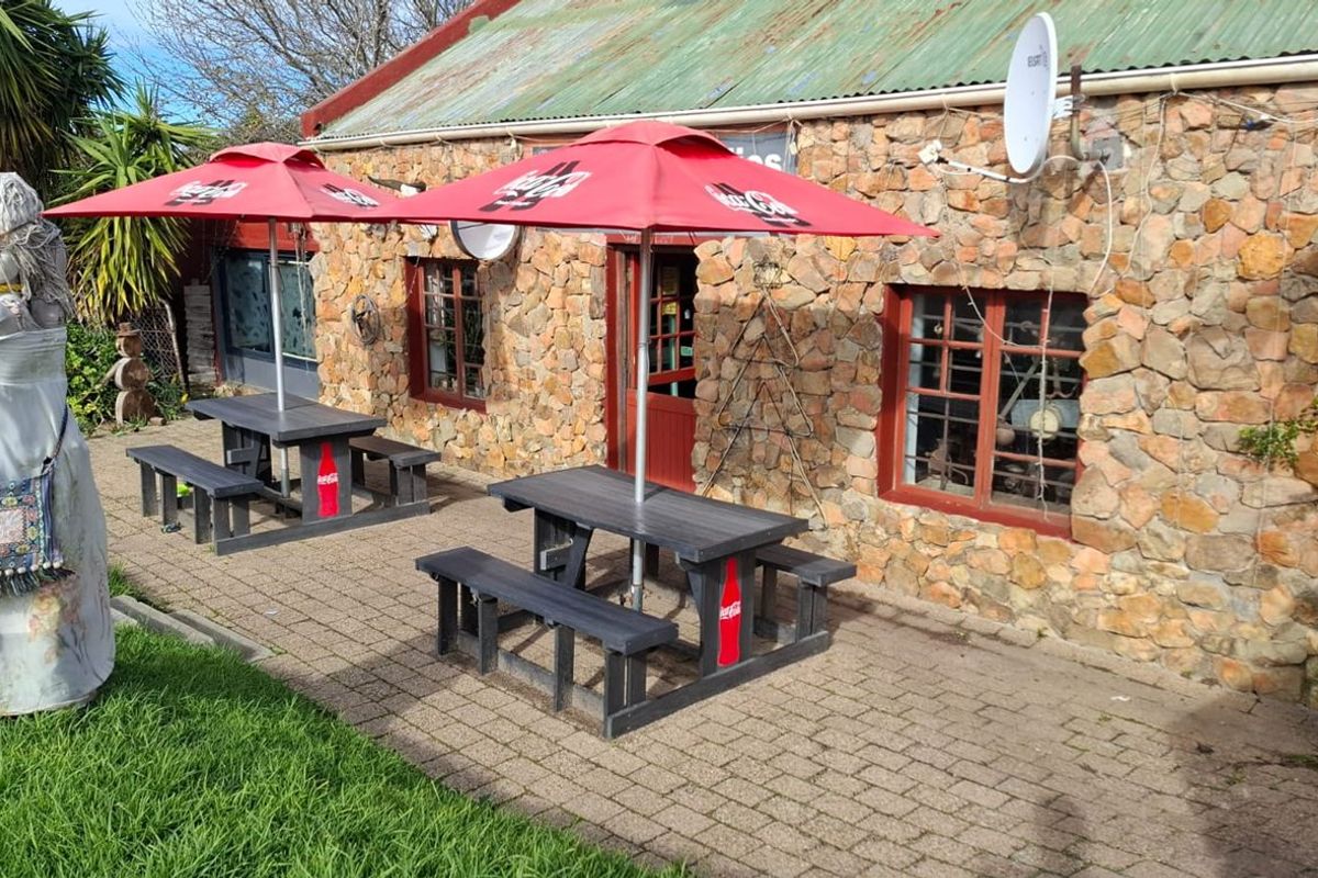 Outdoor patio area featuring stone wall construction, paved flooring, and a corrugated metal roof, providing a rustic exterior seating space for the restaurant.