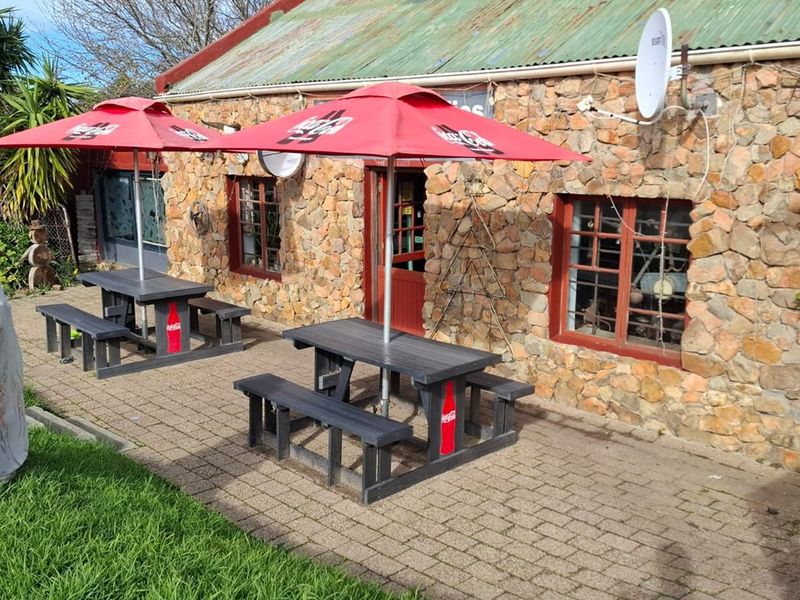 Outdoor patio area featuring stone wall construction, paved flooring, and a corrugated metal roof, providing a rustic exterior seating space for the restaurant.