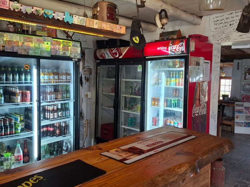 A rustic bar area featuring a wooden counter, exposed timber ceiling beams, tiled flooring, and multiple commercial beverage refrigeration units.