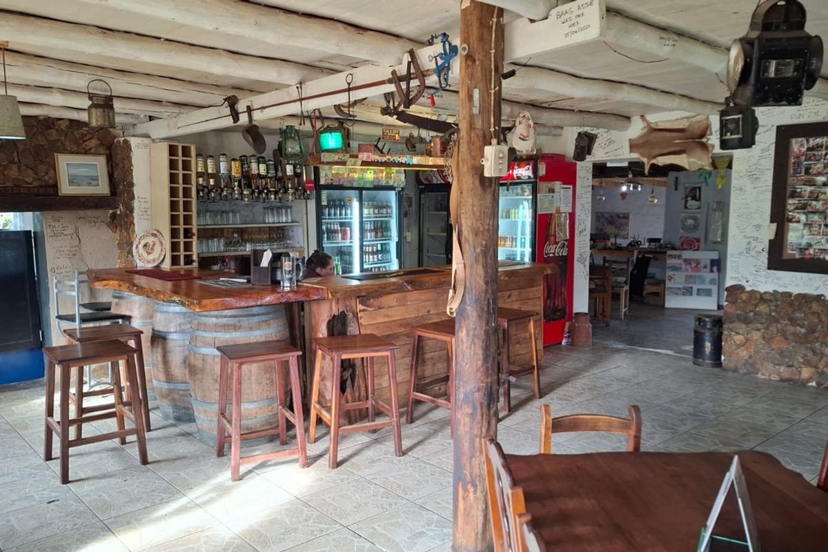 Rustic bar area featuring a wooden counter with barrel supports, exposed timber ceiling beams, and stone wall accents in a casual restaurant setting.
