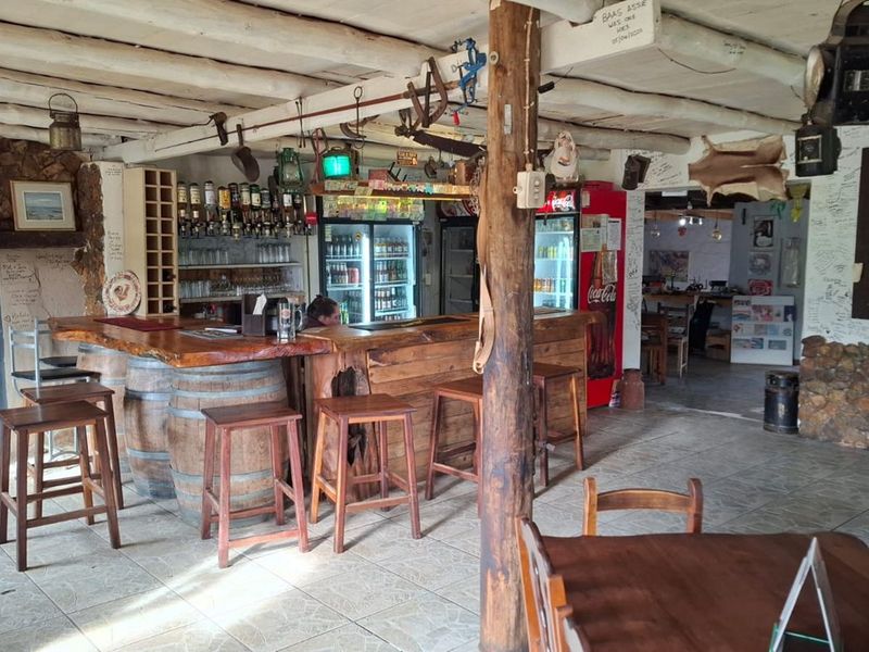Rustic bar area featuring a wooden counter with barrel supports, exposed timber ceiling beams, and stone wall accents in a casual restaurant setting.