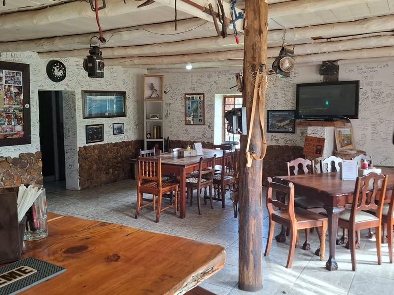 Rustic open-plan restaurant dining area featuring exposed timber beams, stone wall accents, and tiled flooring, currently decorated with extensive wall writing.