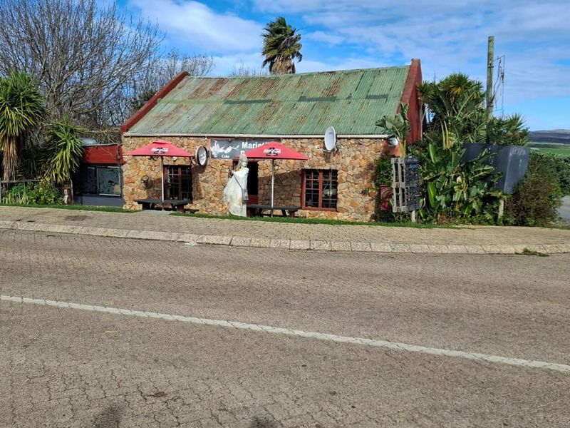 A rustic stone-walled restaurant building featuring a corrugated metal roof, situated on a corner lot with established landscaping.