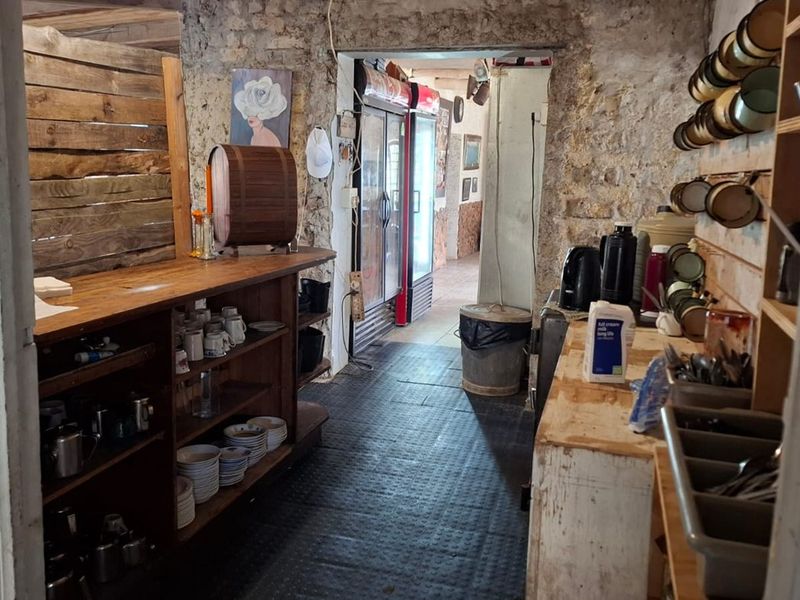 A functional scullery or prep area featuring exposed stone walls, built-in wooden shelving, and commercial refrigeration units, suitable for restaurant back-of-house operations.