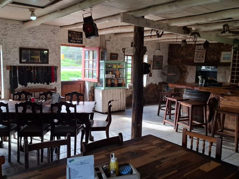 Rustic open-plan restaurant interior featuring exposed timber ceiling beams, a stone feature wall, and a built-in wooden bar counter with tiled flooring.